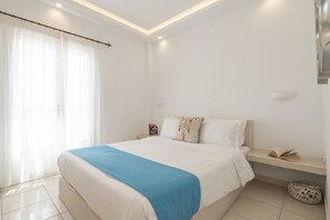 A bedroom with a bed, a bedside table, a lamp, a window with curtains, and a wall-mounted light fixture. - Apartment Sea View BB 3 guests in a family hotel (Perivolos)
