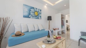 A modern living room with a blue sofa, a painting of a daisy, a lamp, a tray with a bottle and glasses, and a fruit plate. - Apartment Sea View BB 3 guests in a family hotel (Perivolos)