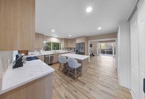 A modern kitchen with a marble countertop, wooden cabinets, and a stainless steel refrigerator.