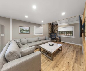 Un salon moderne avec un canapé d’angle, une table basse, une cheminée et une grande fenêtre.
