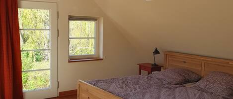 A bedroom with a sloped ceiling, a skylight, a bed, a nightstand, and a window.