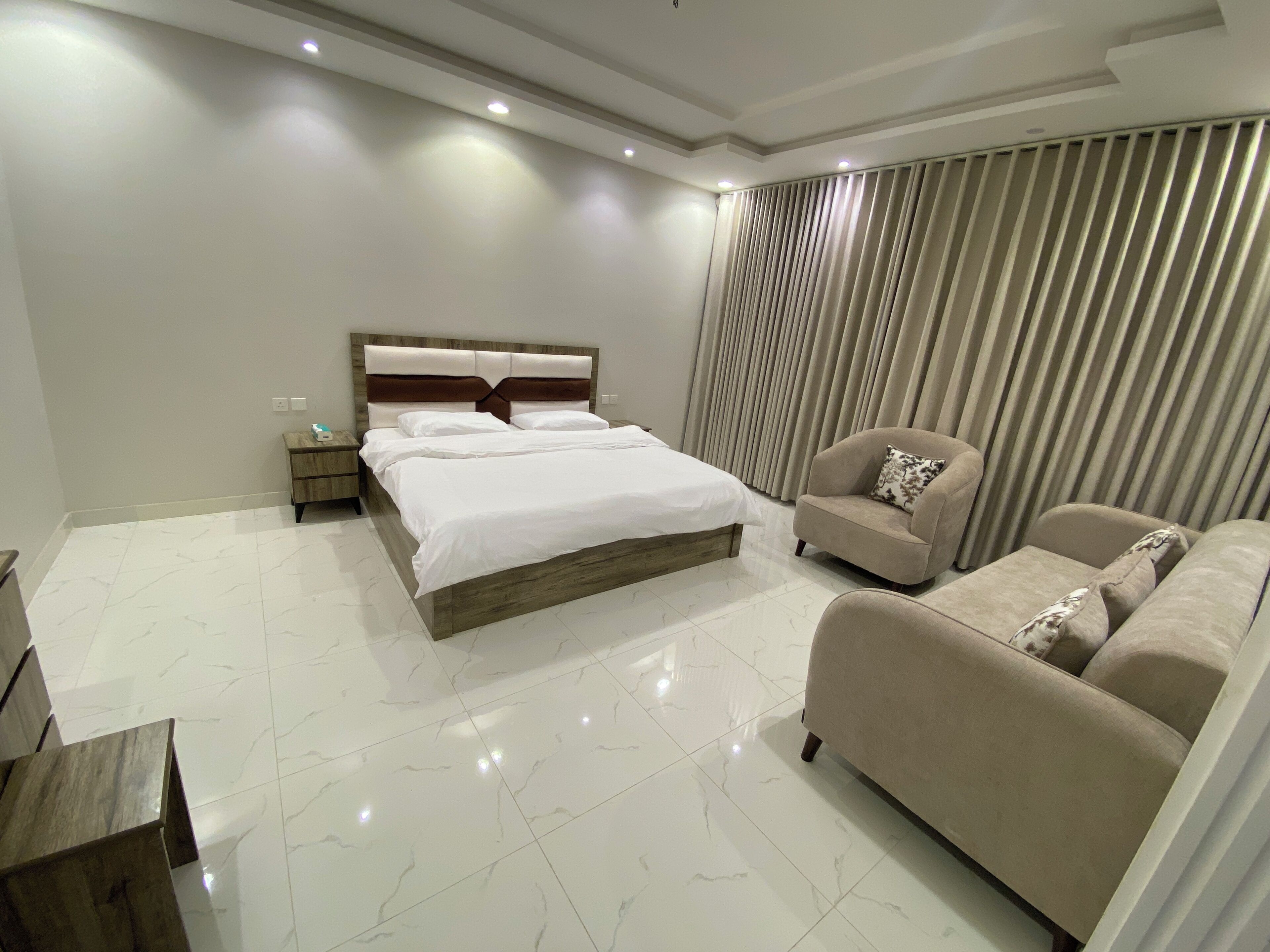 A modern bedroom with a large bed, a sofa, a nightstand, and a window with curtains.