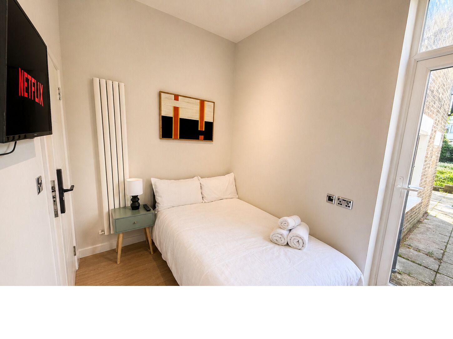 A hotel room with a bed, a bedside table with a lamp, a TV, and a painting on the wall.