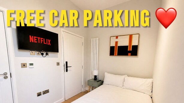 Habitación de hotel con una cama, un televisor mostrando Netflix, un cuadro en la pared y un letrero que indica estacionamiento de coches gratuito.