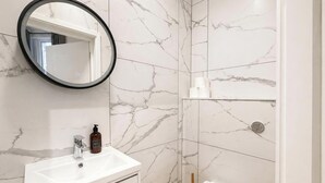 A bathroom with a white sink, a mirror, and marble walls. - Central Studio in the Heart of Hounslow! (Greater London)