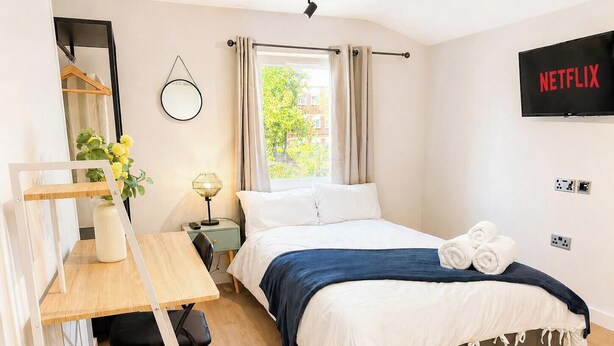 Un dormitorio con cama, escritorio, silla, televisor y ventana con cortinas.