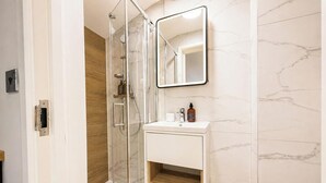 Un baño con ducha de vidrio, un lavabo blanco con encimera de mármol y un espejo sobre el lavabo.