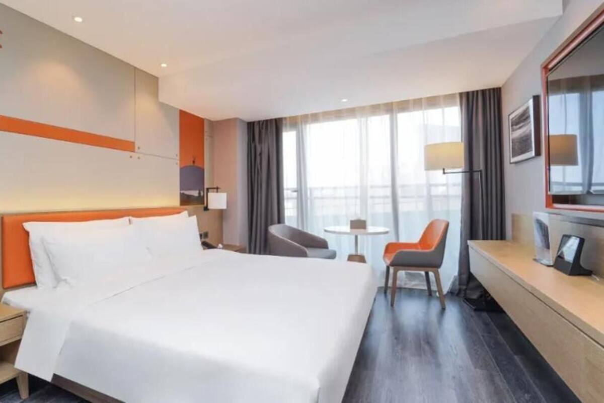 Habitación de hotel con una cama grande, un escritorio, una silla, una mesita y un televisor.