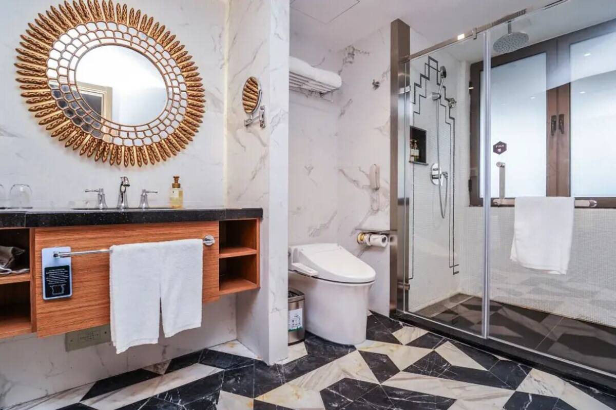 Un baño moderno con suelo de mármol, un espejo redondo, un inodoro y una ducha con mampara de vidrio.