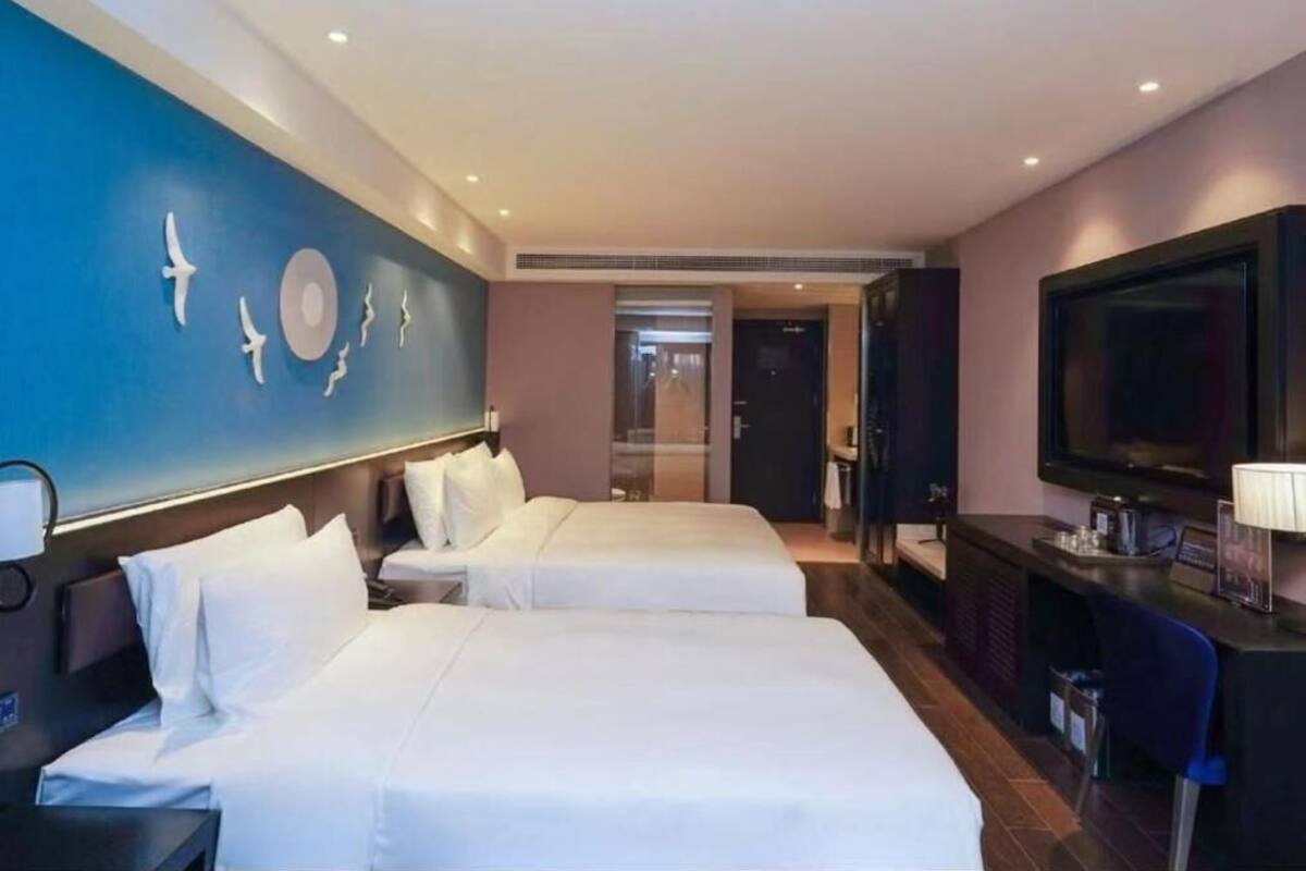 Habitación de hotel con dos camas, televisión, escritorio y pared decorada.