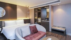Et moderne hotelværelse med en stor seng, en sofa, et lille bord og et badeværelse, der kan anes gennem en åben dør.