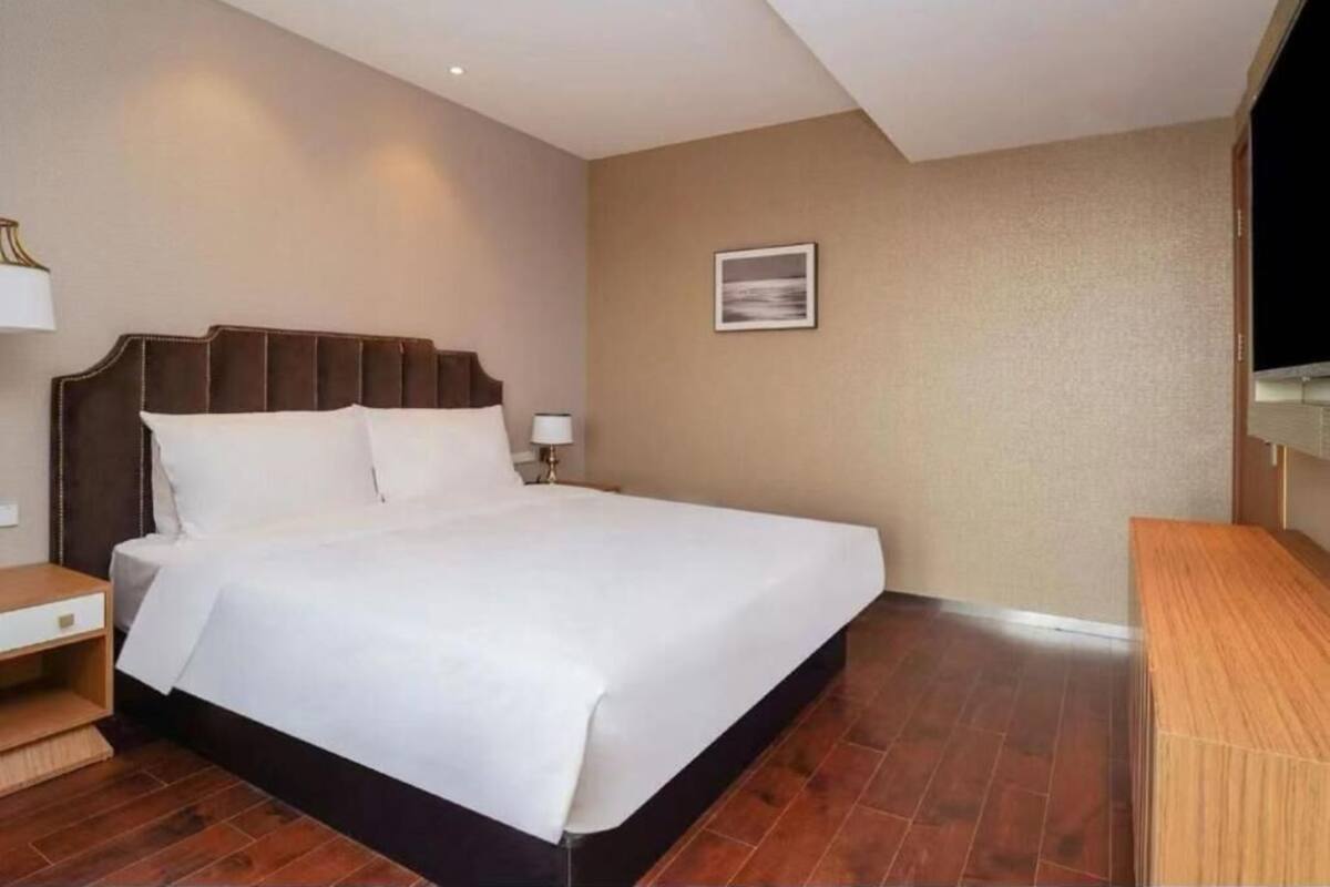 Una habitación de hotel con una cama grande, una mesita de noche, un escritorio y un televisor montado en la pared.