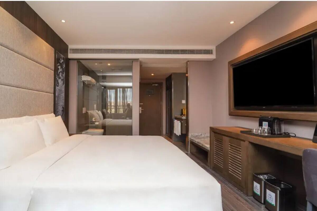 Una habitación de hotel con una cama grande, televisión, escritorio y baño visible a través de una puerta abierta.