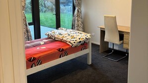 Een slaapkamer met een bed, een bureau en uitzicht op een tuin.