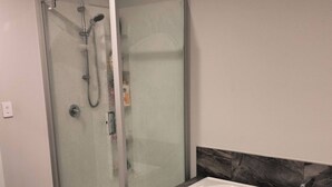 Een moderne badkamer met een douchecabine, een wit bad en marmeren accenten aan de wand.