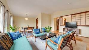 Ein Wohnzimmer mit Sofa, Sesseln, Couchtisch, Fernseher und einer Schiebetür.