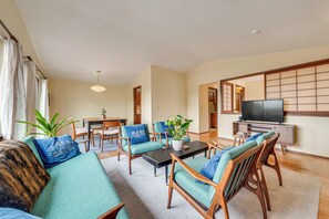 A living room with a sofa, chairs, a coffee table, a TV, and a sliding door. - Steps to Great Food, Bus Routes & Light Rail (Seattle)