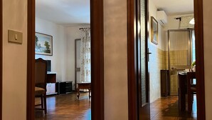 A hallway with patterned wooden flooring, a dining area with a table and chairs, and a kitchen area with a refrigerator and sink. - Casa Genziana Sabbiadoro - Terrace - Parking - Air conditioning (Lignano Sabbiadoro)