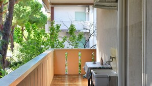 A balcony with a tiled floor, a table with a tablecloth, a chair, and a window overlooking greenery. - Casa Genziana Sabbiadoro - Terrace - Parking - Air conditioning (Lignano Sabbiadoro)