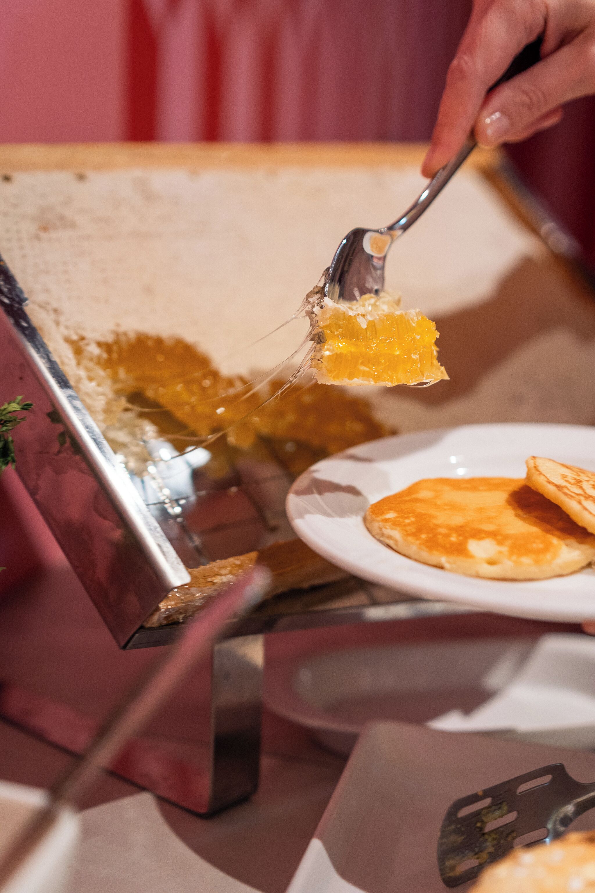 A hand holding a spatula with a piece of food, a plate with pancakes, and a metal container.