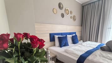 A hotel room with a bed, a table with a bottle and glass, and a vase with red roses.