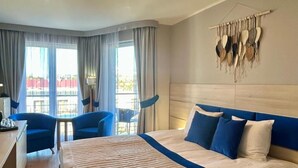 Hotellihuone, jossa on suuri sänky, työpöytä, kaksi tuolia ja suuret ikkunat, joista avautuu näkymä kaupunkiin.