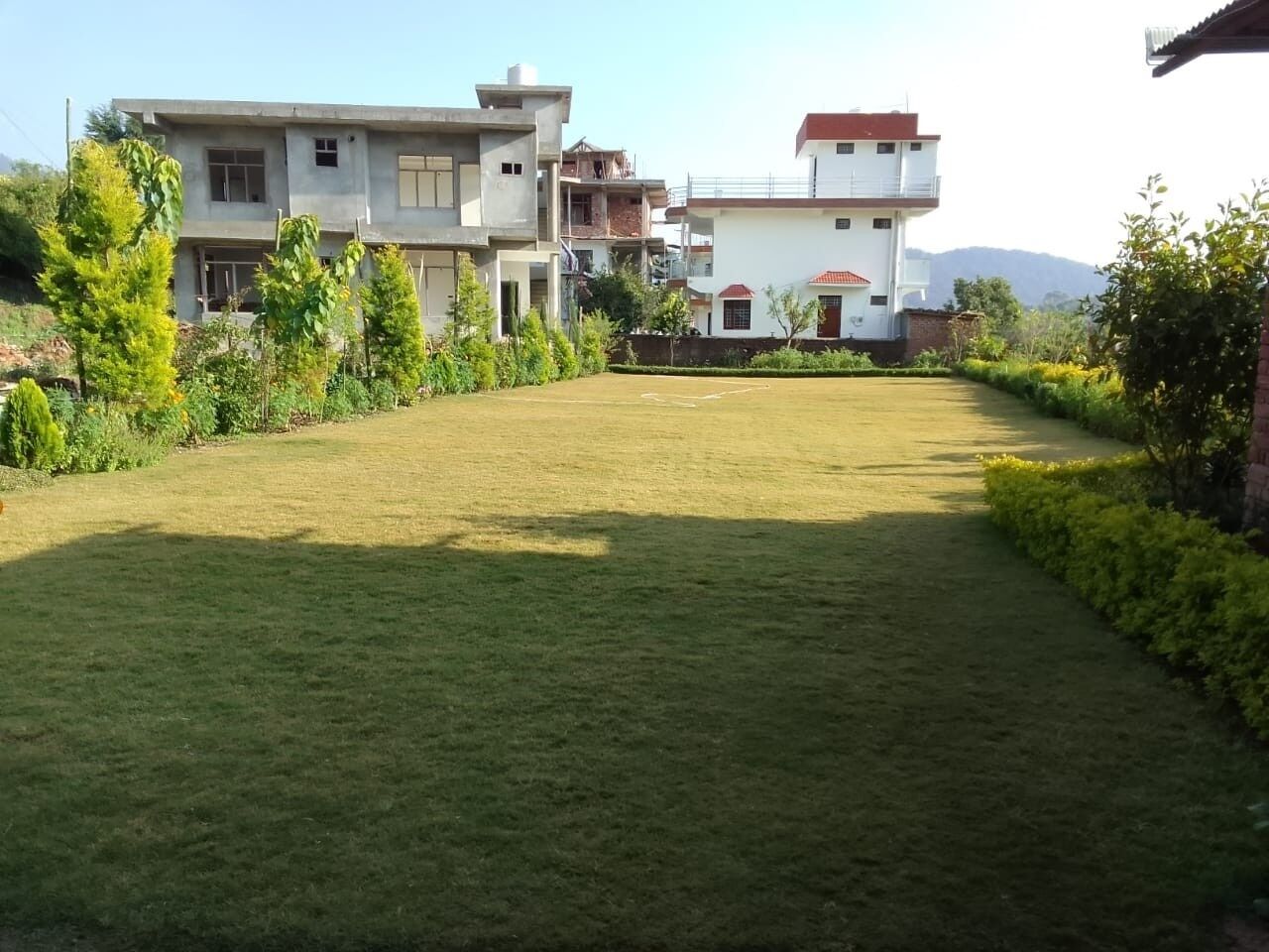 A residential area with two multi-story houses, a well-maintained lawn, and surrounding greenery.