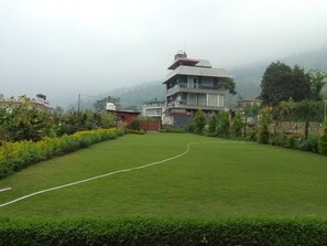 A grassy area with a white line, surrounded by greenery and buildings in the background. - Celestial Rhapsody 3 BR, Naukuchiatal (Dungsil Malla)