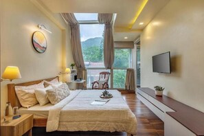 A bedroom with a bed, bedside lamps, a TV, a window with curtains, and a view of greenery outside. - Celestial Rhapsody 3 BR, Naukuchiatal (Dungsil Malla)