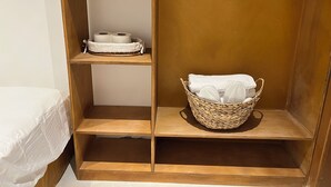 A wooden shelf unit with a basket containing a white towel and a roll of toilet paper.