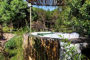 Ein Whirlpool, umgeben von üppiger Vegetation, einer Steinmauer und einem Bambuszaun.