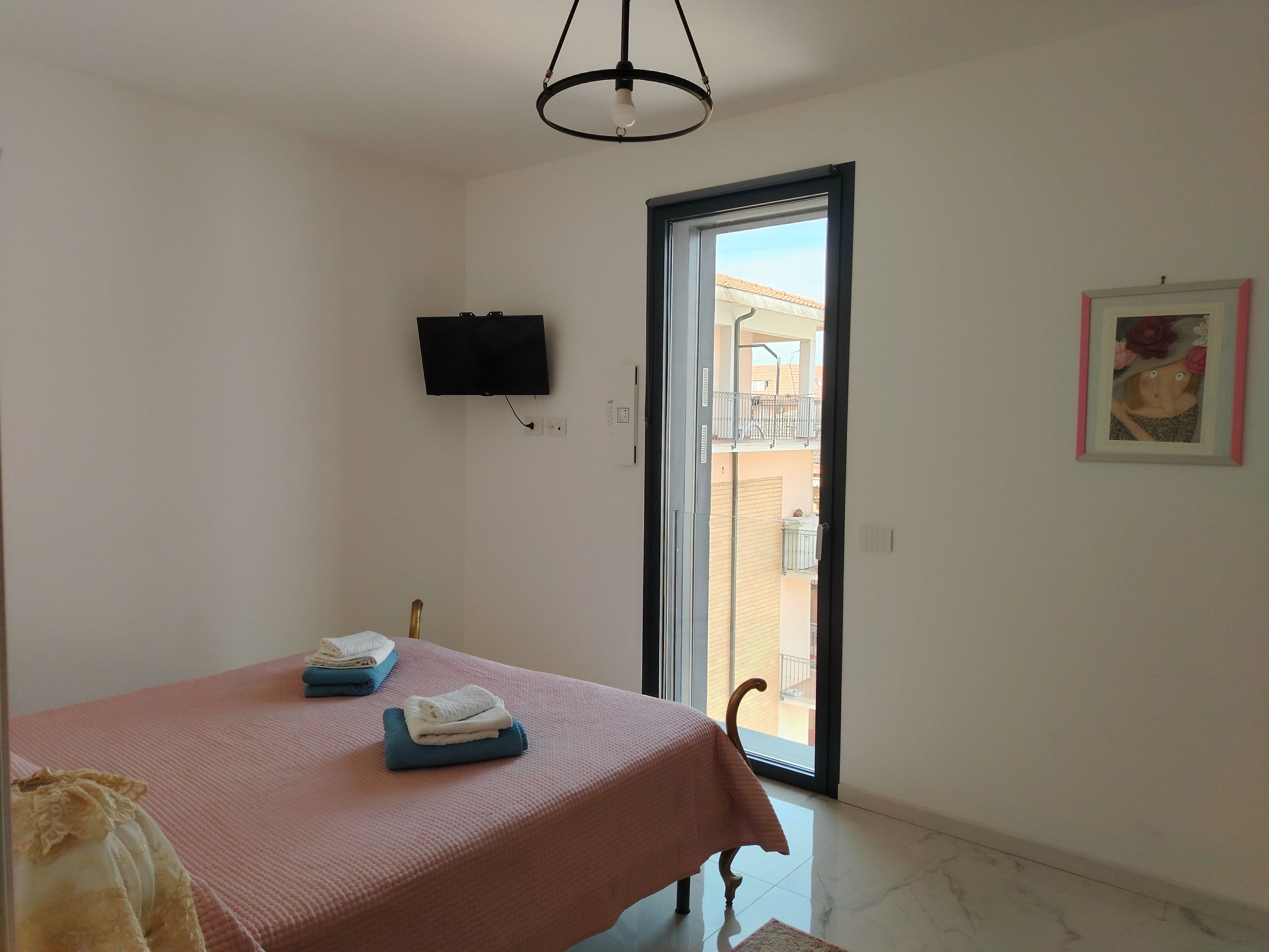Ein Schlafzimmer mit einem Bett, einem Fernseher, einer Tür, die auf einen Balkon führt, und einem gerahmten Bild an der Wand.