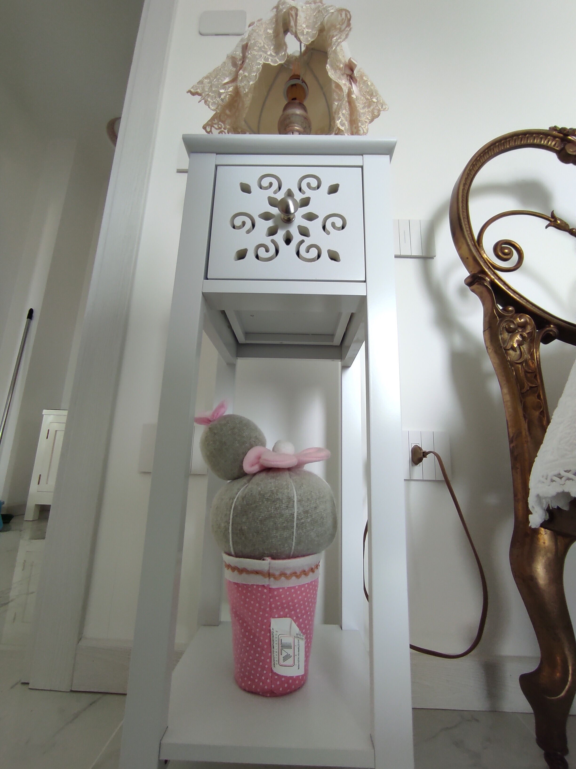 A white shelf with decorative items, a mirror with a gold frame, and a wall socket.