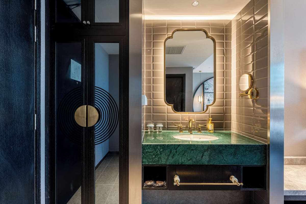 Un baño moderno con lavamanos de mármol, accesorios dorados y un espejo grande.