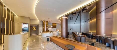 A modern hotel lobby with a reception desk, seating areas, and a staircase.