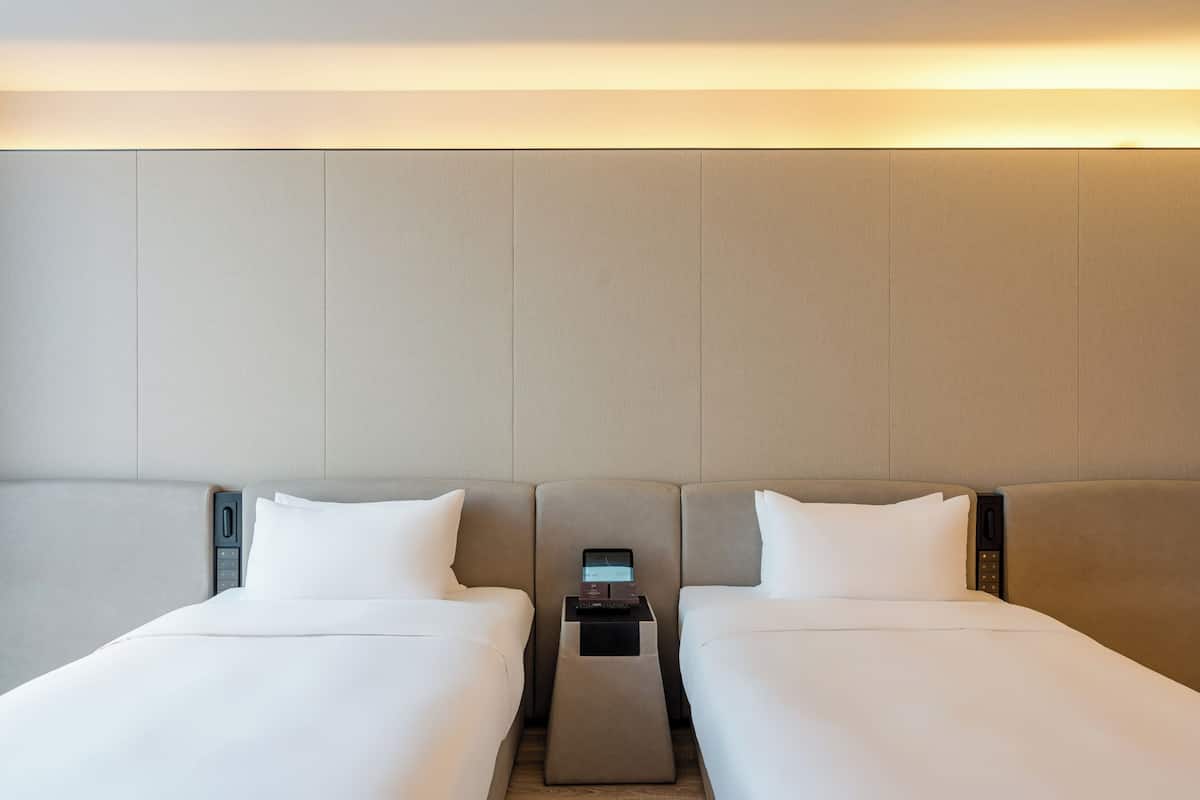 Habitación de hotel con dos camas, una mesita de noche con estación de carga e iluminación integrada en la cabecera.