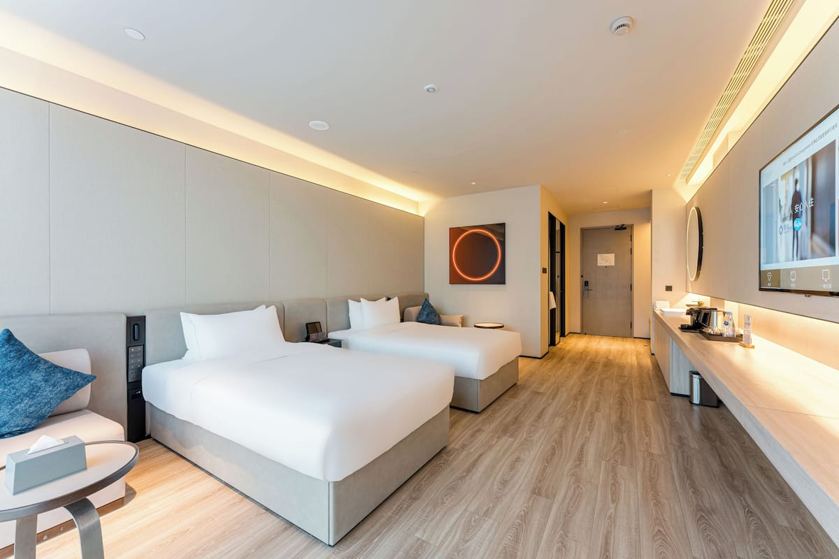 Habitación de hotel con dos camas, un escritorio, una silla y un televisor.