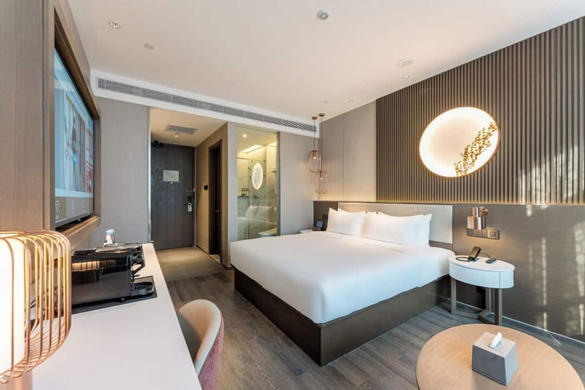 Una habitación de hotel moderna con una cama grande, mesitas de noche, un escritorio con una computadora y un televisor.
