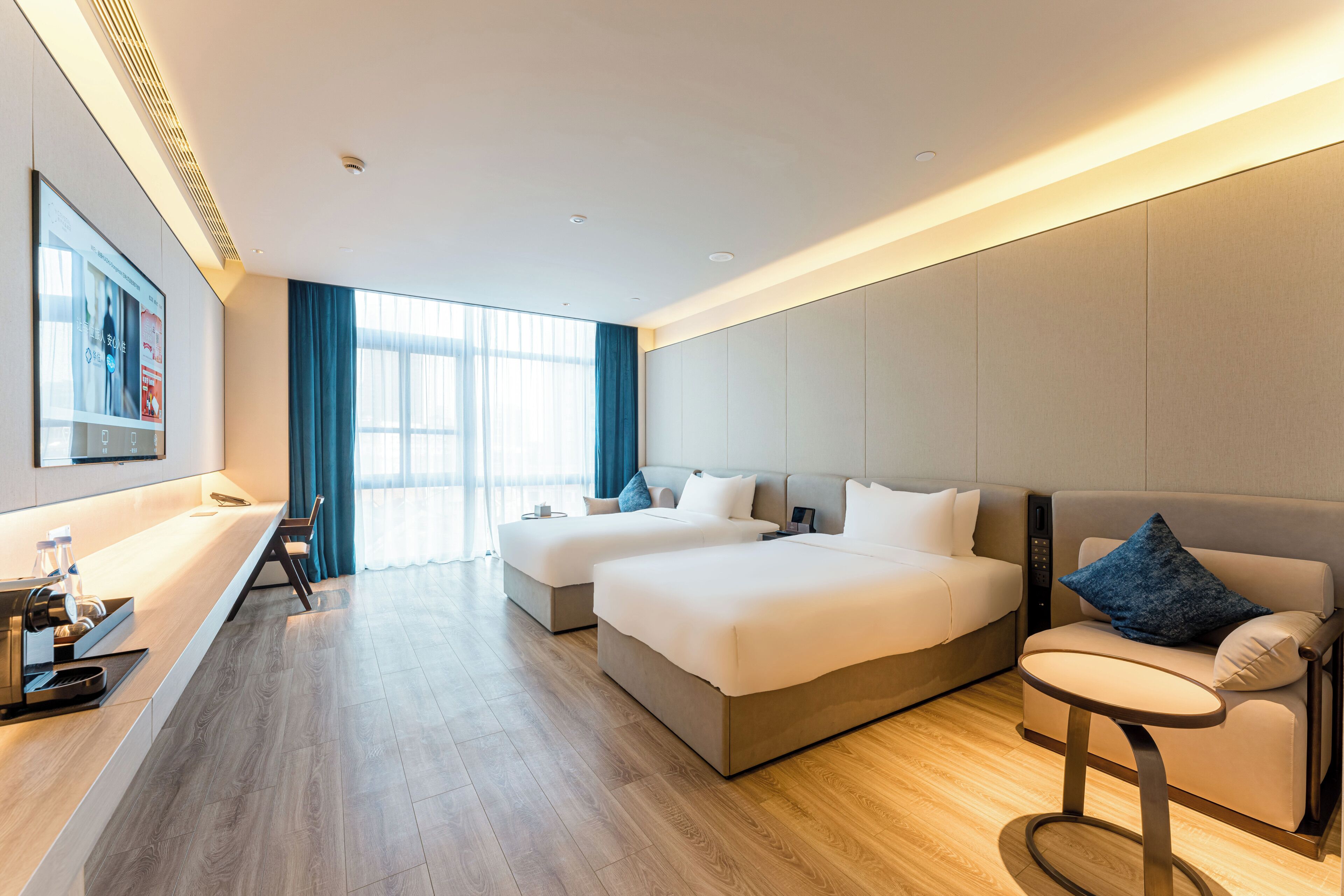 A modern hotel room with two beds, a sofa, a small table, and a TV.