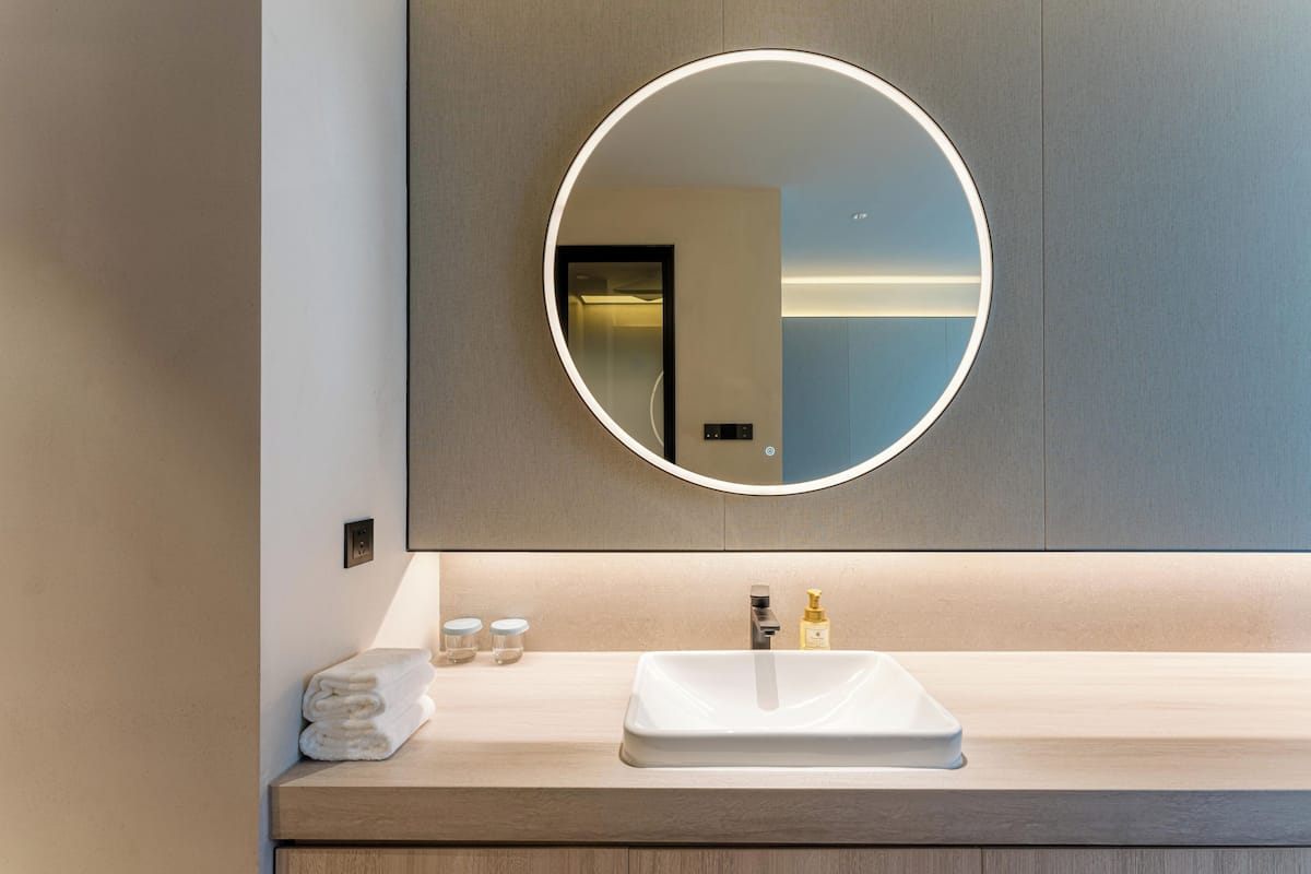 Un baño moderno con un espejo redondo, un lavamanos blanco y un perchero para toallas.