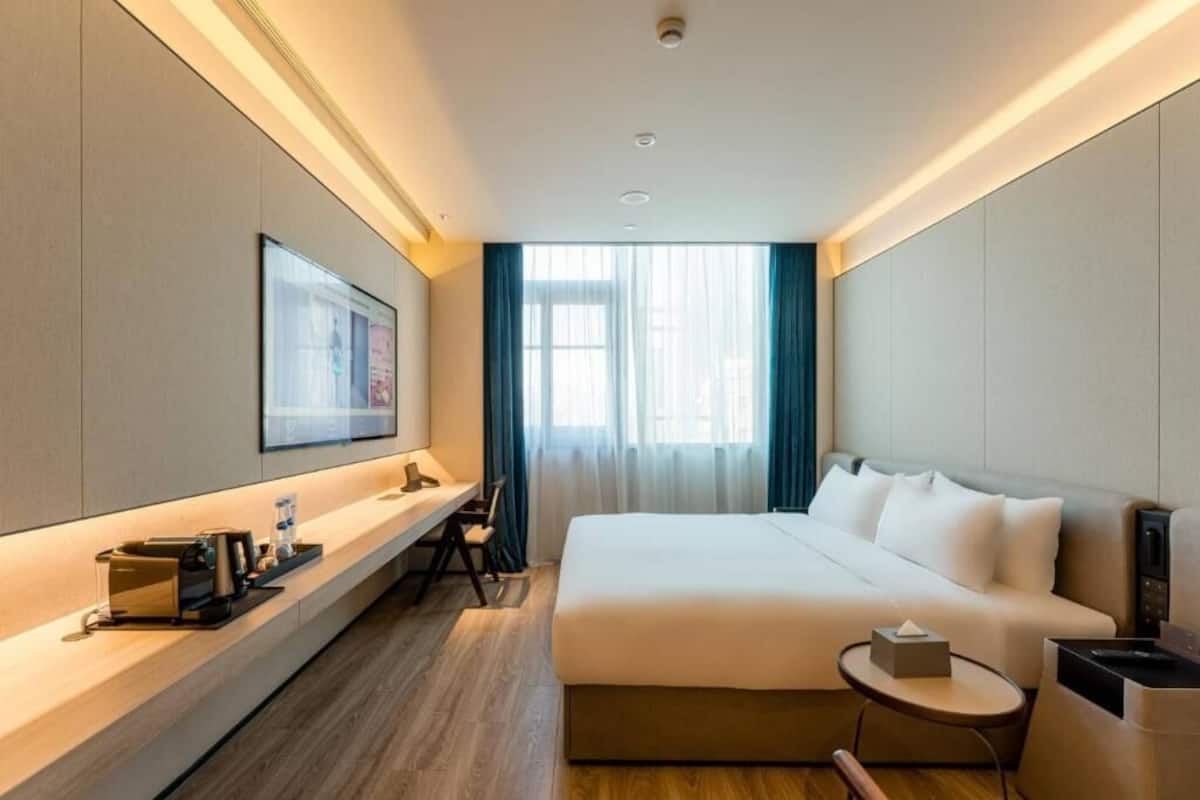 Una habitación de hotel moderna con una cama, mesita de noche, un escritorio con silla, televisor y ventana con cortinas.