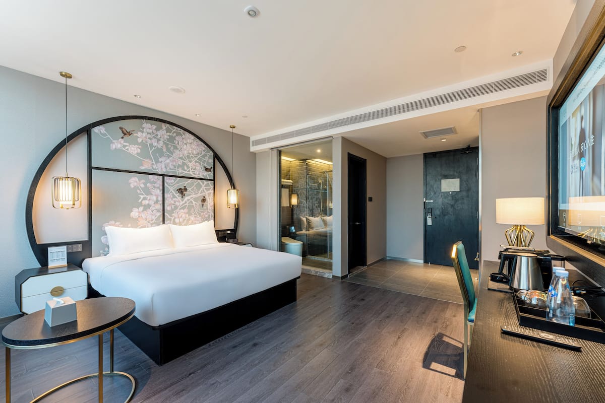 Habitación de hotel moderna con una cama grande, mesita de noche, lámpara y vista al baño.