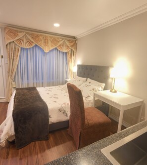 Quarto de hotel com cama, mesa de cabeceira, abajur e um pequeno banco.