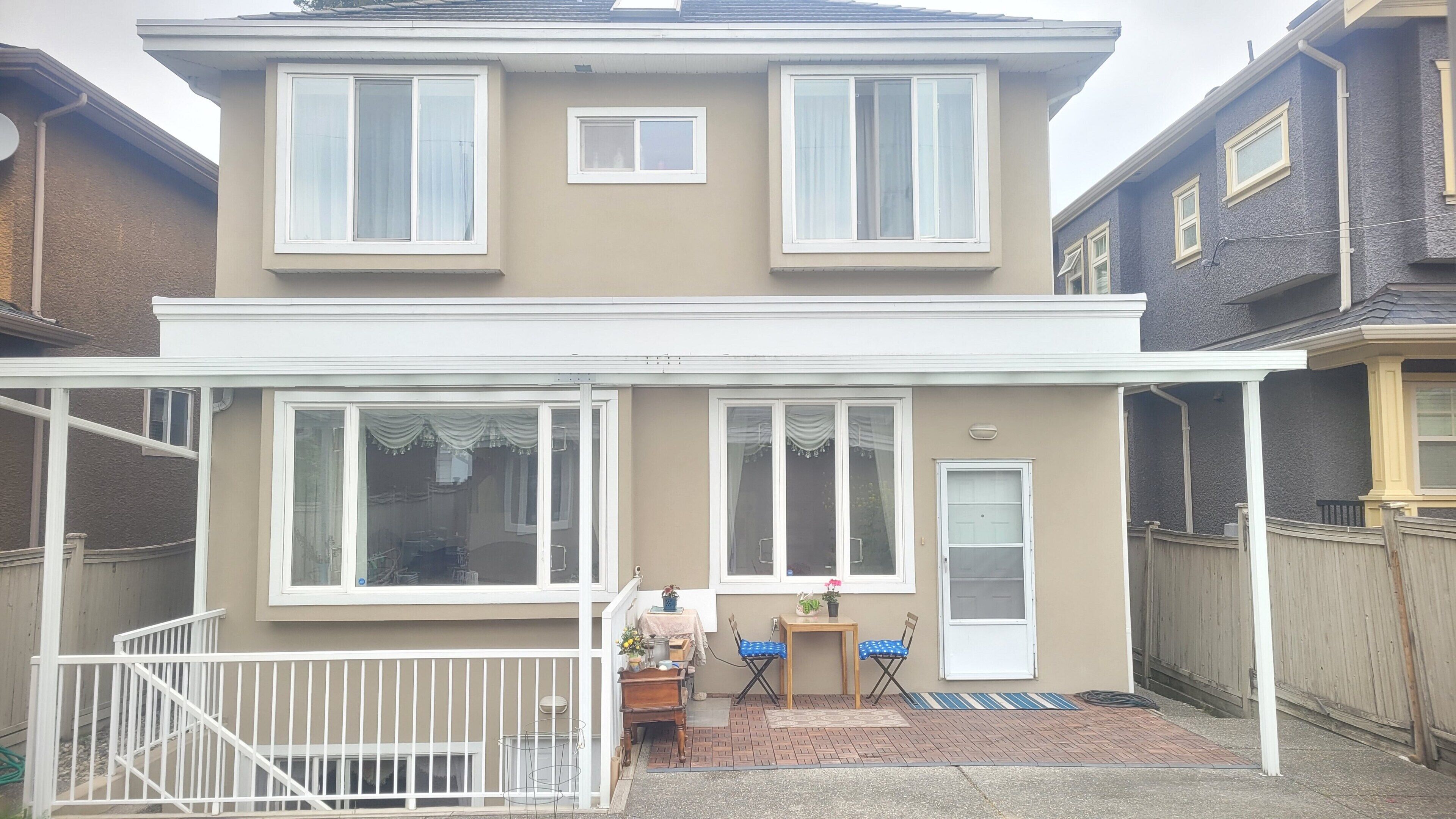 A two-story house with a covered patio, a small table with chairs, and a fenced yard.