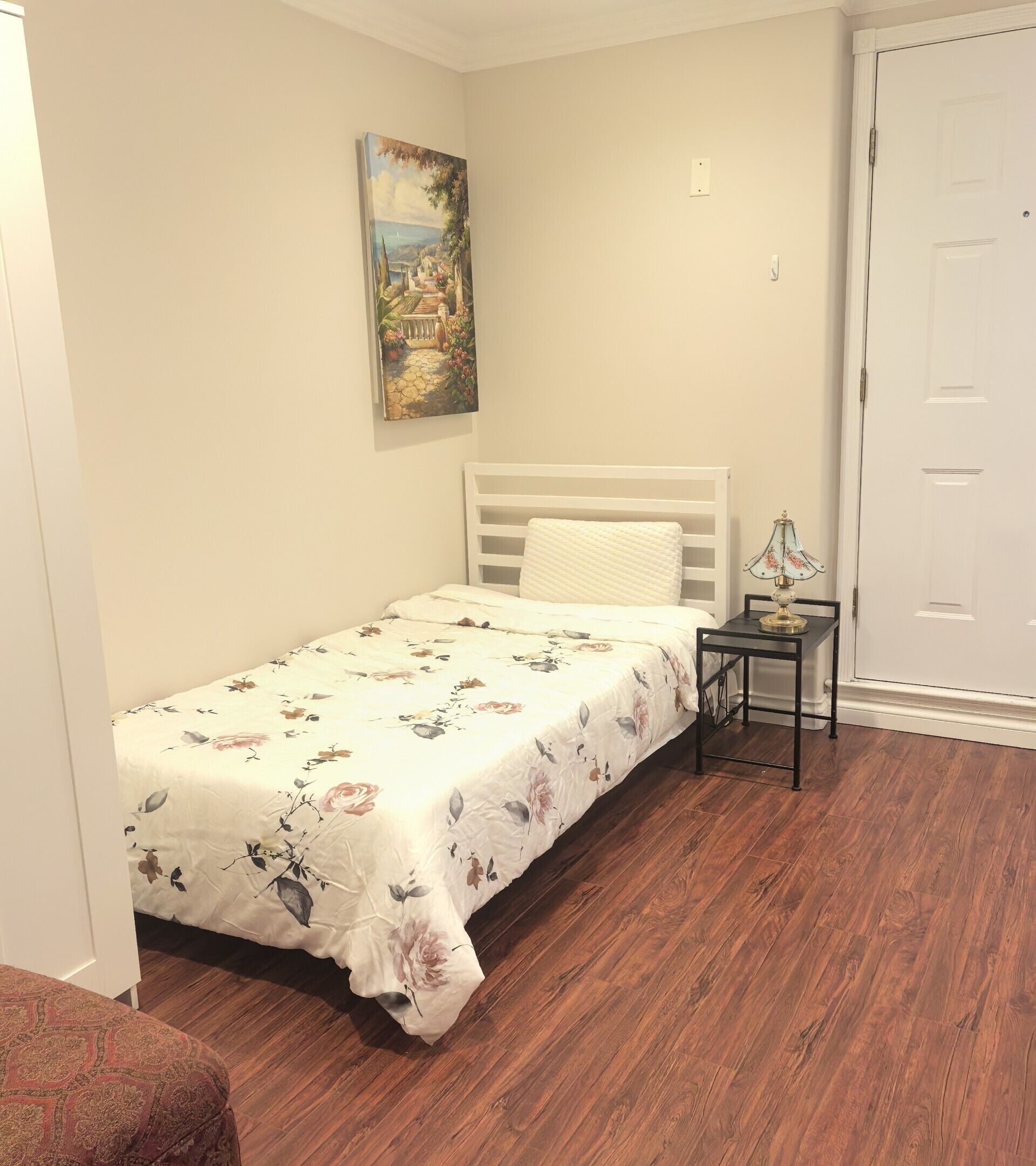 Une petite chambre à coucher avec un lit simple, une table de chevet, une lampe et un tableau au mur.