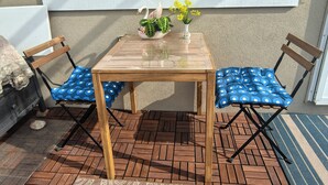 A wooden table with two blue polka-dotted chairs, a potted plant, and yellow flowers on a patio with a herringbone-patterned floor. - Sunshine Home Vancouver Near UBC/DT/YVR  Family-sized Studio (Vancouver)
