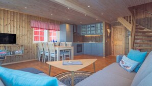 L’intérieur chaleureux d’un chalet comprend un coin repas, une cuisine et un salon aménagé avec un canapé et des fauteuils.