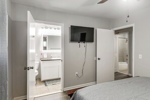 Une chambre à coucher avec un lit, un téléviseur fixé au mur et une porte ouverte donnant sur une salle de bain avec douche.