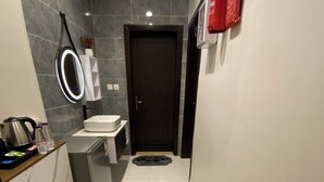 Un baño moderno con una puerta oscura, un lavabo blanco y un espejo con marco iluminado.