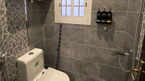 Un baño moderno con inodoro, ducha y un pequeño ventanal.